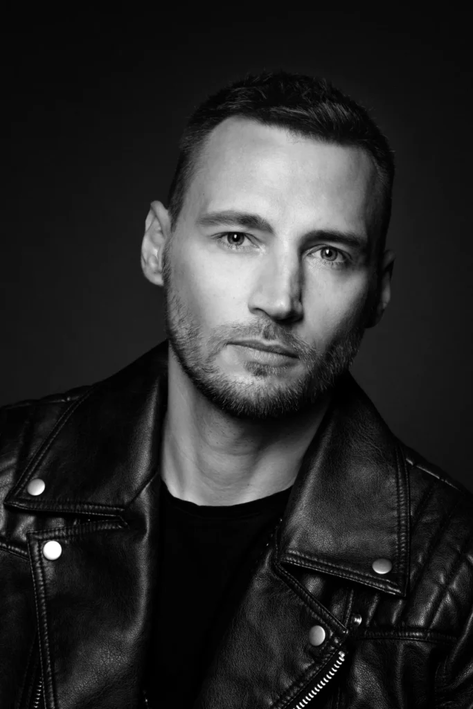Portfolio aktorskie - portret młodego mężczyzny aktora czarno - biały. Mężczyzna aktor - spogląda niepokojąco do kamery Fotograf Natalia Rakowska